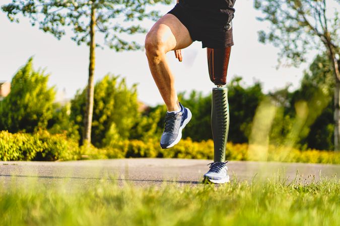 Crop view of athletic man with prosthetic leg exercising outdoors in the parkland