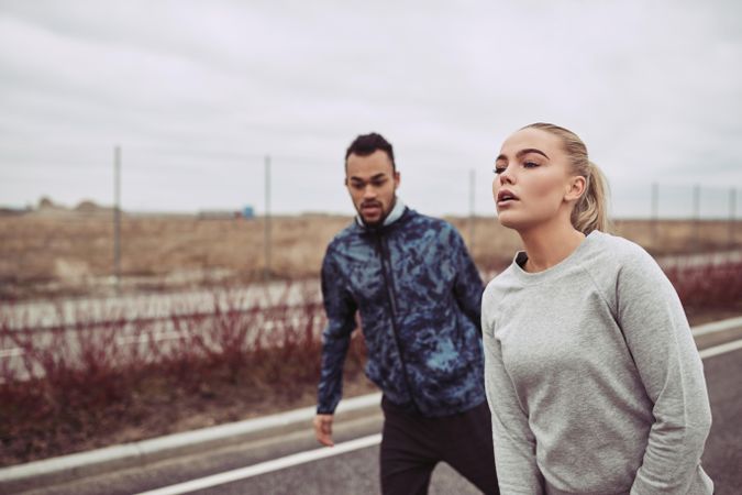 Athletic woman and man preparing to start run on empty country road