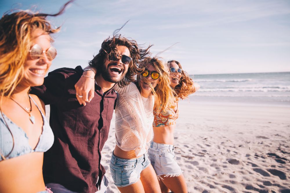 Group of friends smiling and laughing walking along the the beach