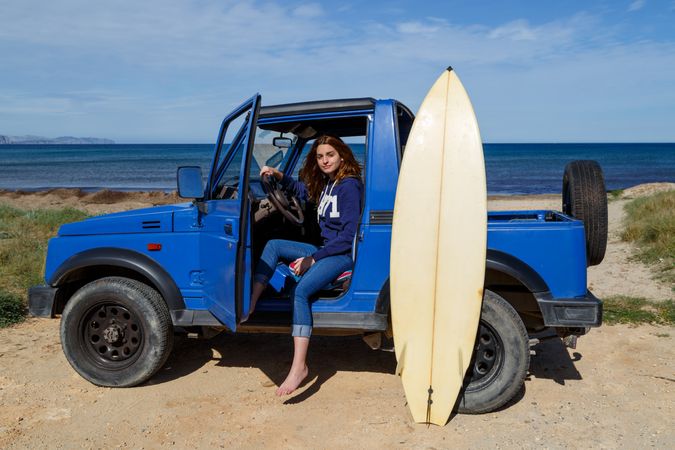 Woman sitting in car with surfboard at seaside
