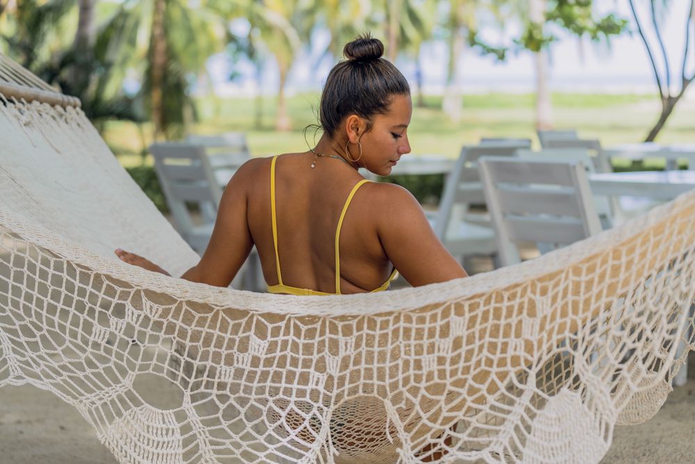 Joyful woman in bikini resting in hummock on beach