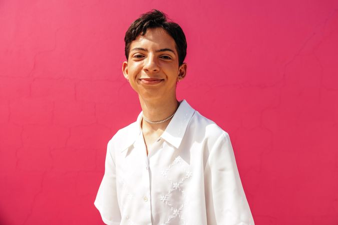 Smiling young man in light shirt  standing against a pink background