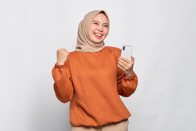 Elated Muslim woman looking happy holding her smartphone