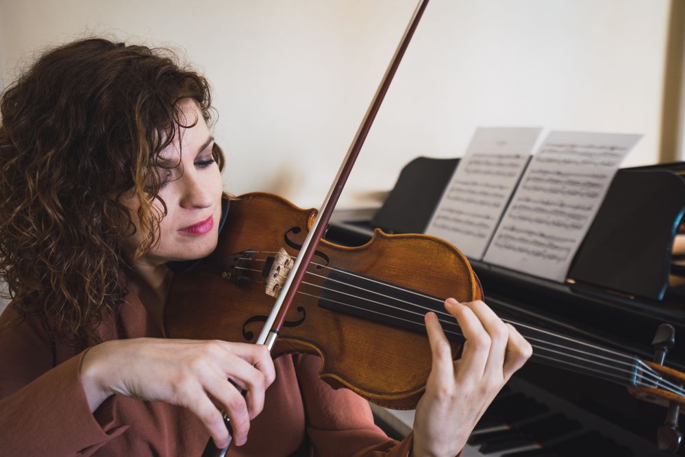 Pregnant woman playing on violin near piano in room