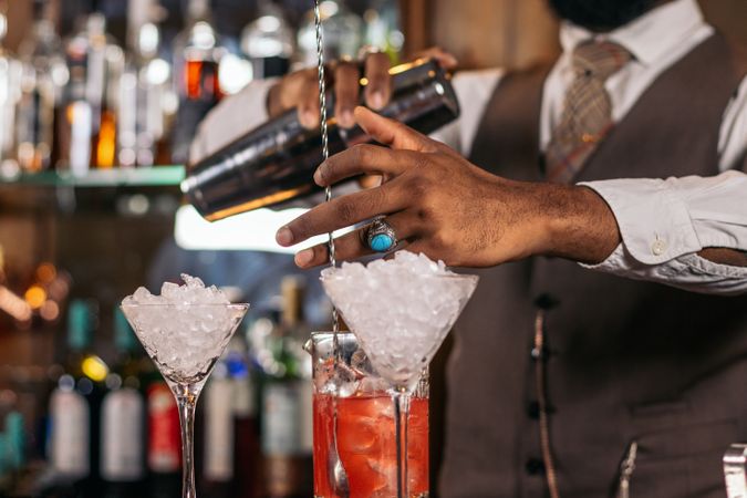 Close-up of the hands of a stylish Black bartender preparing a cocktail in a shaker in a traditional cocktail bar