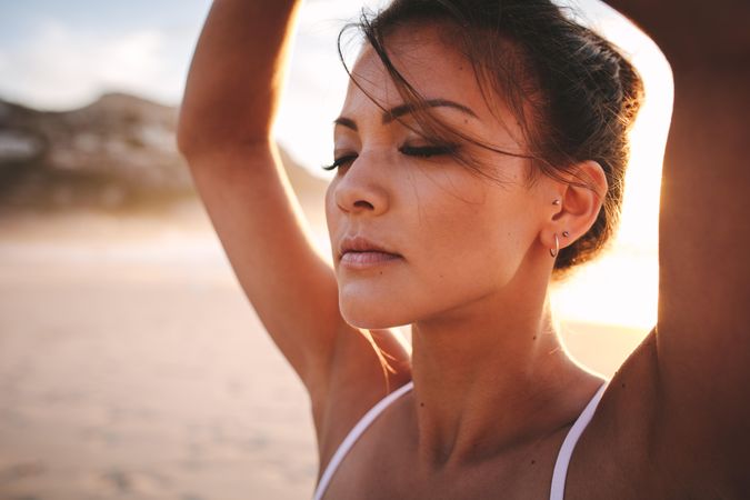 Close up of fit woman sitting on beach with eyes closed