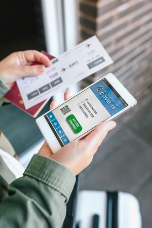 Unrecognizable woman holding cell phone with covid passport and
