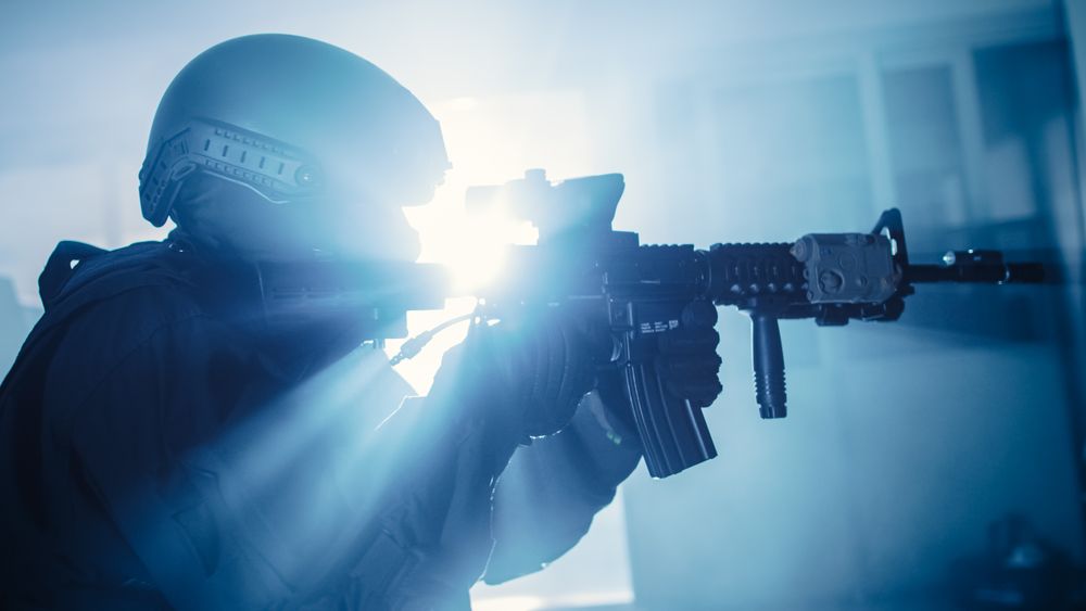 Close Up Portrait of Masked Squad Member of Armed SWAT Police Officers Who Storm a Dark Seized Office Building with Desks and Computers
