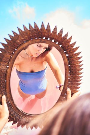 Romantic female in swimwear reflecting in mirror on shore