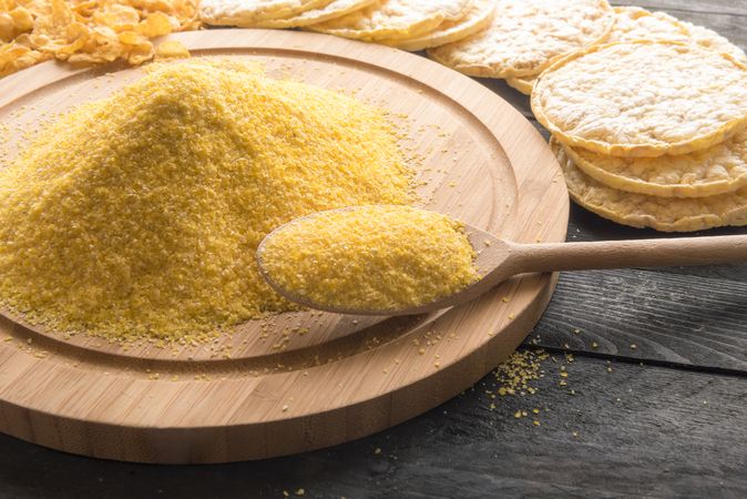Wooden spoon with cornmeal near a pile of flour on a rustic table