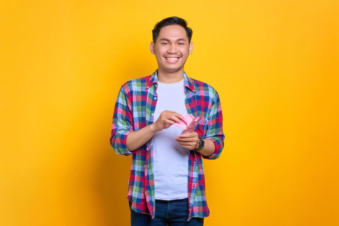Smiling happy Asian man holding cash in studio shoot