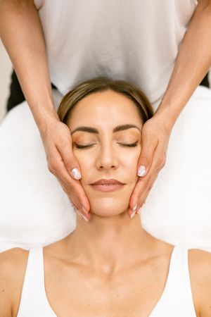 Looking down at woman having her face massaged by massage therapist, vertical