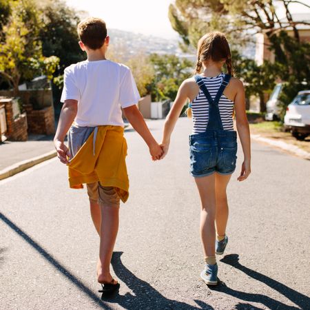 Rear view of a boy and girl walking on an empty street while holding hands