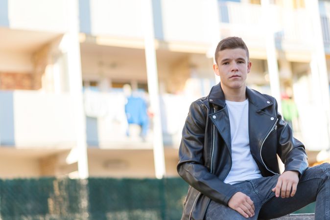 Teenage male wearing a leather jacket sitting outside