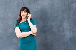 Thoughtful female on the phone against a gray wall