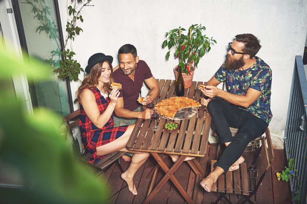 Three friends on a rooftop patio with pizza and wine