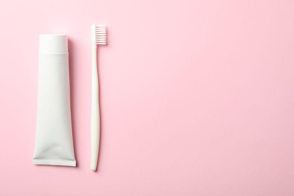Toothbrush and toothpaste on pink background, space for text