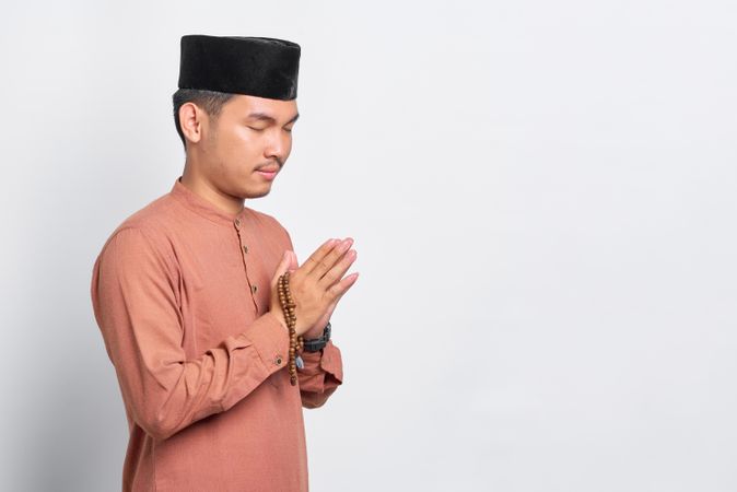 Muslim man in kufi head wear with his hands pressed together in prayer