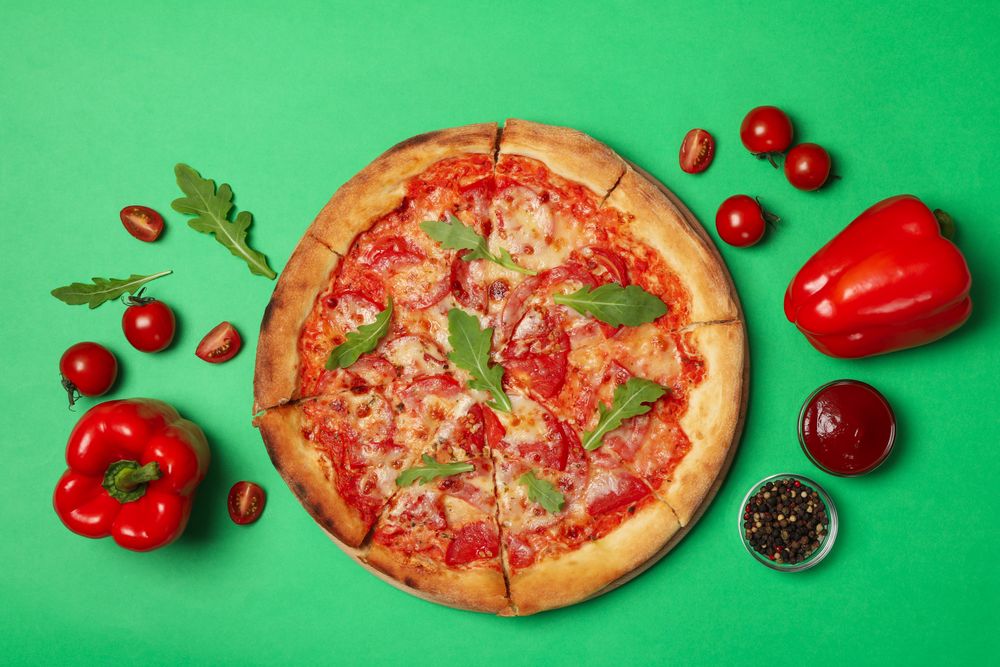 Tasty pizza and ingredients on green background