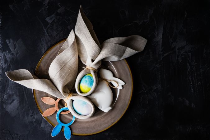 Easter eggs wrapped with rabbit ears with napkin with nest on dark table