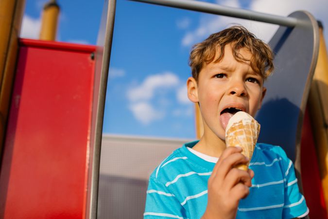 Close up of a boy eating an ice cream sitting on a slide