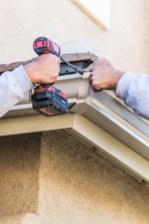 Workers Attaching Aluminum Rain Gutter to Fascia of House