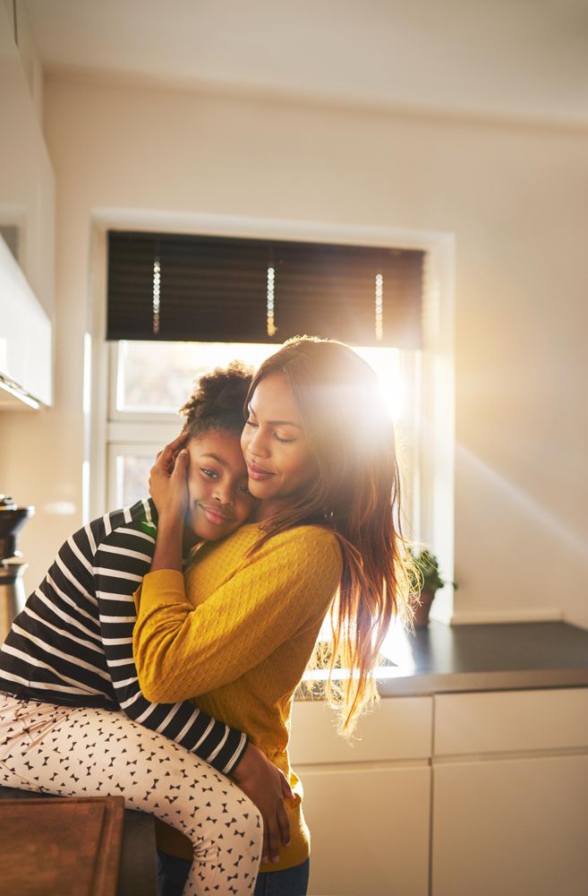 Daughter rests on mother’s chest in bright kitchen