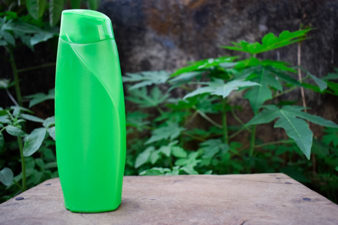 Green shampoo bottle on ledge with hedge behind