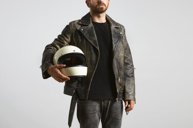 Man in leather jacket holding motorcycle helmet on light background