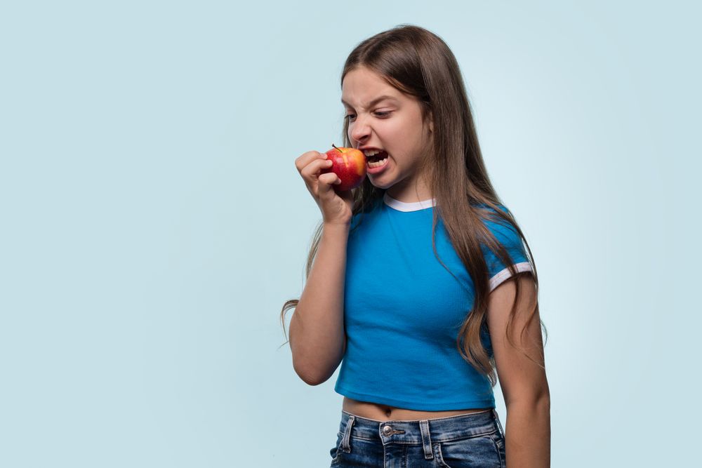 Young girl bites into red apple with playful expression.