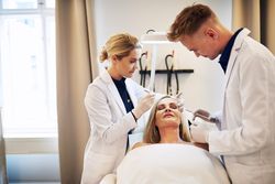 Two dermatologists injecting treatment into patient