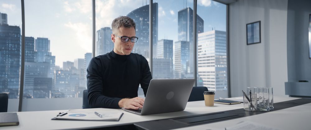 Businessman Standing In Corner Office And Holding Laptop Infront Big Window With Megapolis Cityview.