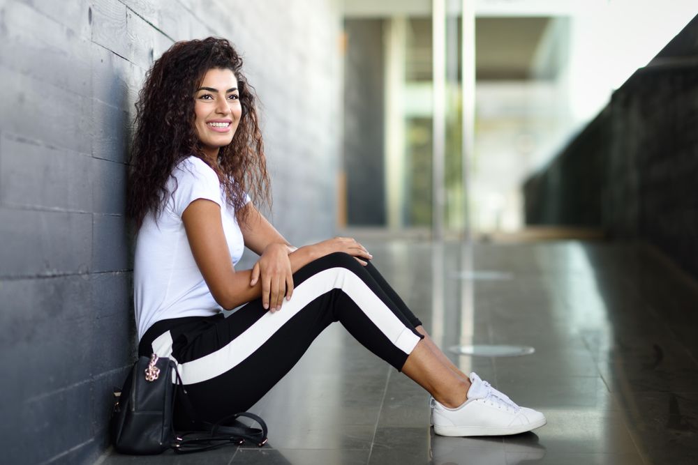 Happy female in leggings sitting outside of building entrance