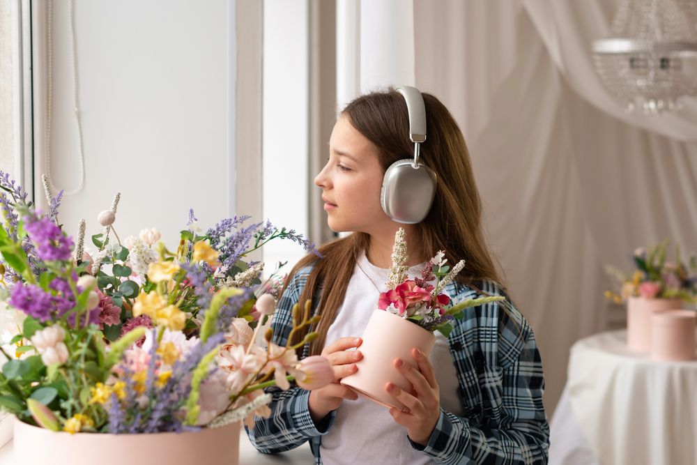 Teen girl wearing headphones holding flowerpot by sunny window.