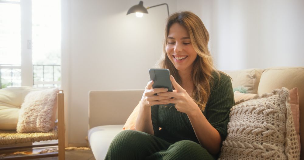 Portrait of Female Using Smartphone in Stylish Living Room while Resting on Cozy Couch Sofa.