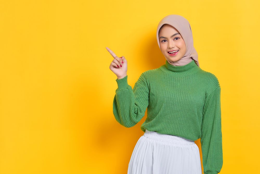 Woman in headscarf pointing up at yellow copy space