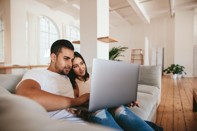 Young man and woman relaxing on couch watching video on laptop