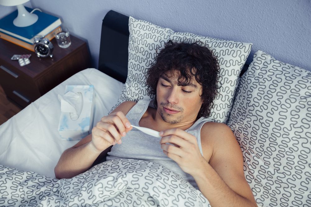 Looking down at sick man with tissues checking temperature in bed