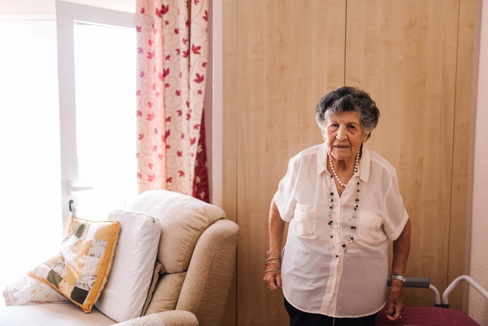 Older woman standing near armchair at home