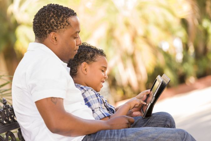 Black Father and Son Using Touch Pad Computer Tablet Outside