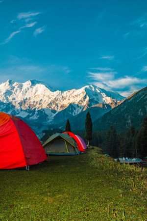 Red tents camping facing snow capped mountains in Pakistan, vertical composition