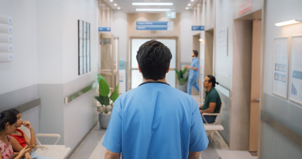 Backview Shot of Young Male Doctor Walking in Hospital Corridor.