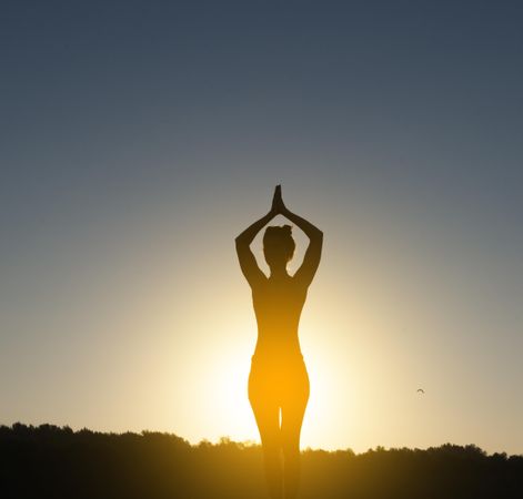 Silhouette of woman standing with arms up in yoga pose during sunset