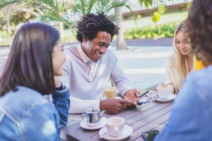 Friends smiling and laughing at joke over coffee and juice at outside table
