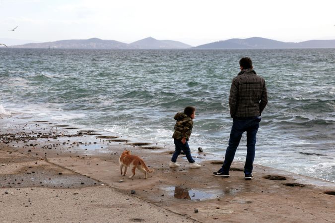 Father and son standing by shoreline during winter