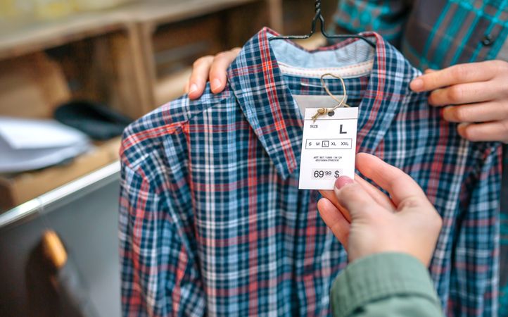 Close up of unrecognizable woman client hand holding label of plaid shirt on clothing shop