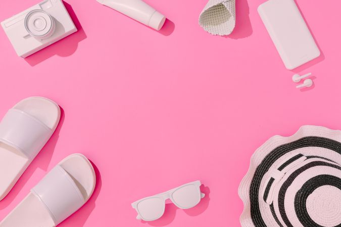 Summer objects of flip flops, sunglasses, camera, smart phone, hat and EarPods on pink background