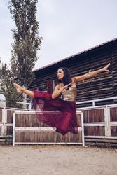 Expressive woman in colorful skirt dancing at rural paddock