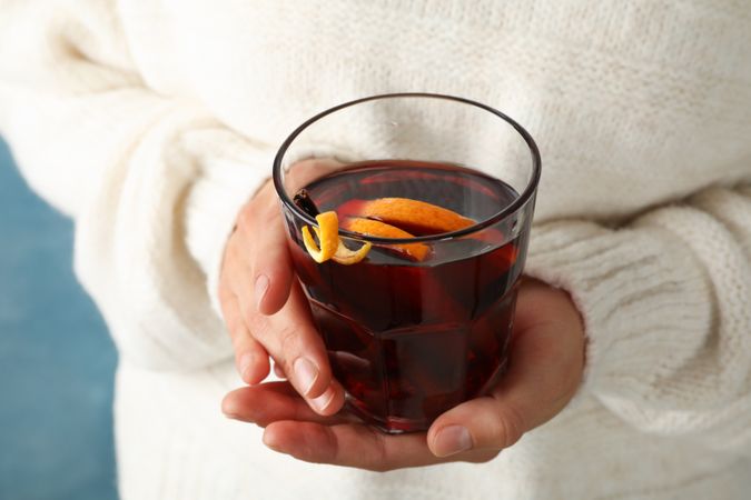 Girl in sweater holding glass with mulled wine, close up