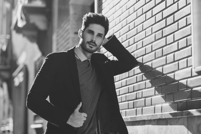 Man leaning on brick wall outside wearing elegant suit, b&w